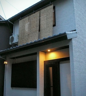 Traditional architecture with a tiled roof and textured facade, featuring a wooden door and air conditioning unit.