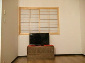 Una habitación con un armario de madera, un televisor encima y un celosía japonesa arriba.