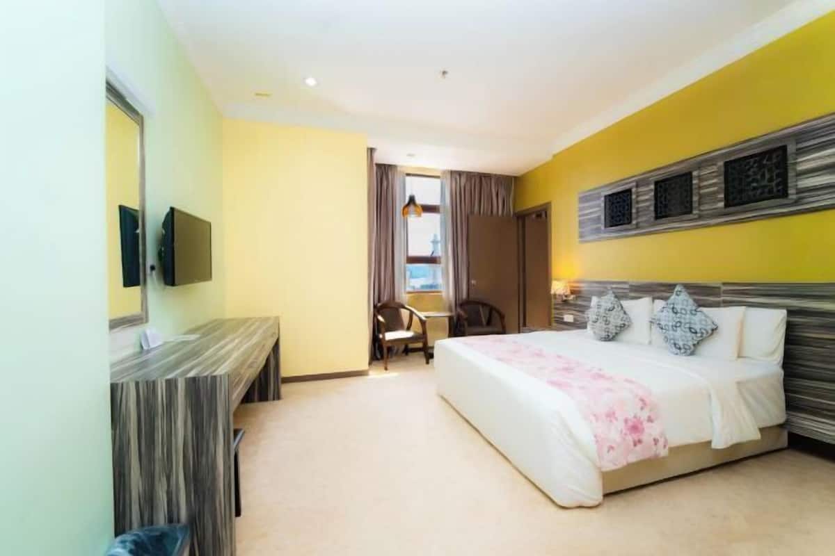 A hotel room with a bed, a desk, a chair, a TV, and a window with curtains.