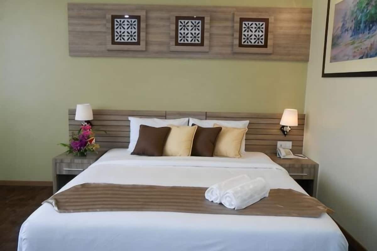 A hotel room with a large bed, two bedside tables, a wall-mounted telephone, and decorative wall panels.