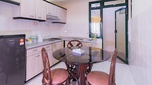 A compact kitchen with a refrigerator, stove, and dining table with chairs. -  Istana Residences Langkawi (Langkawi)