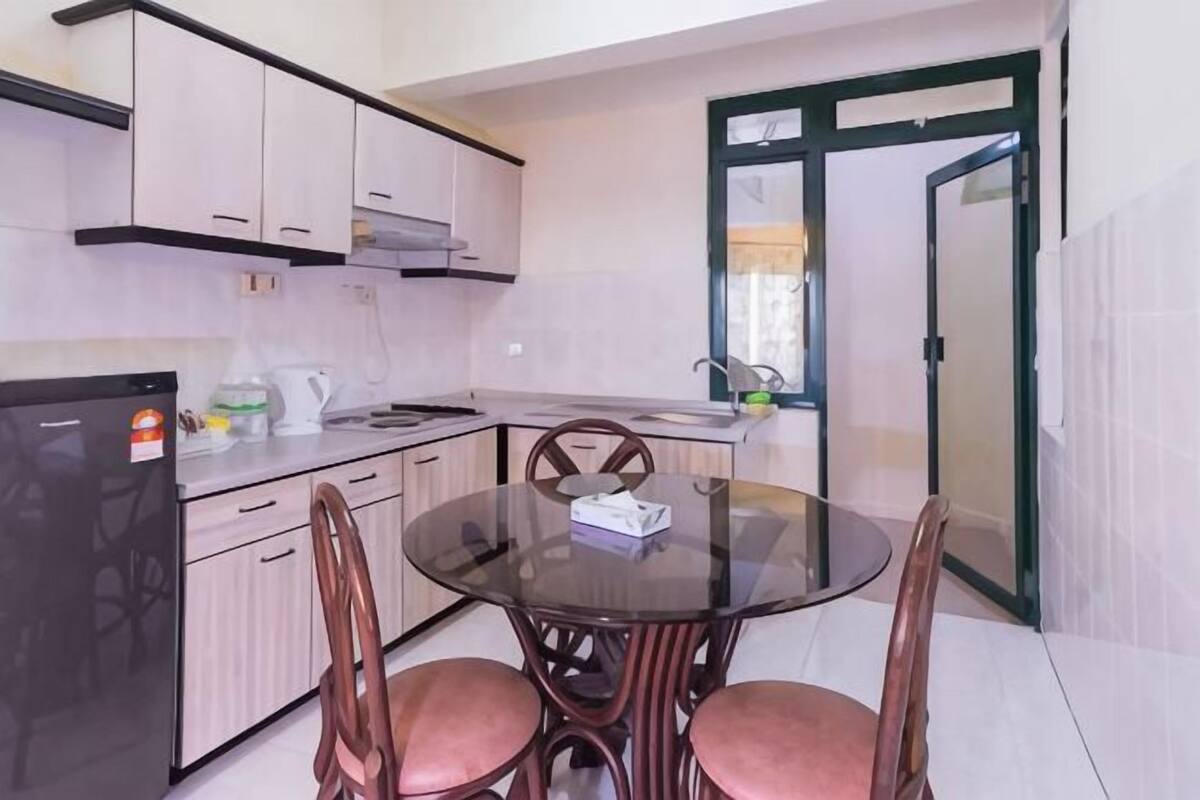 A compact kitchen with a refrigerator, a stove, a sink, and a glass-top dining table with four chairs.