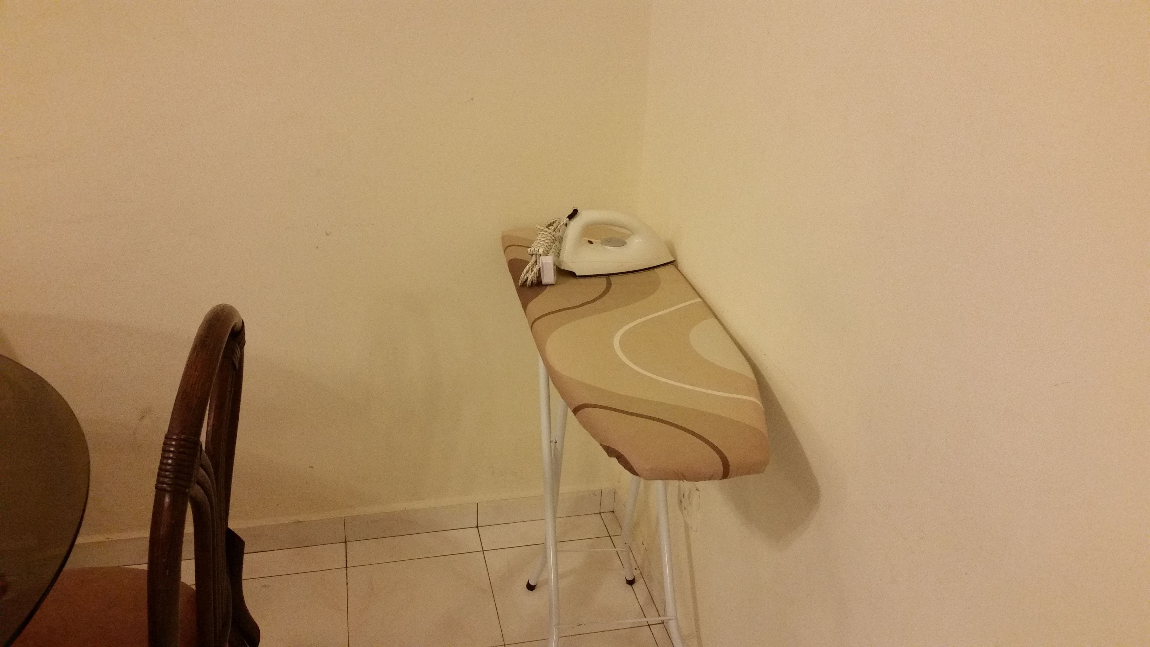 Een strijkplank met een strijkijzer en een doek, geplaatst tegen een muur in een kamer met betegelde vloer.
