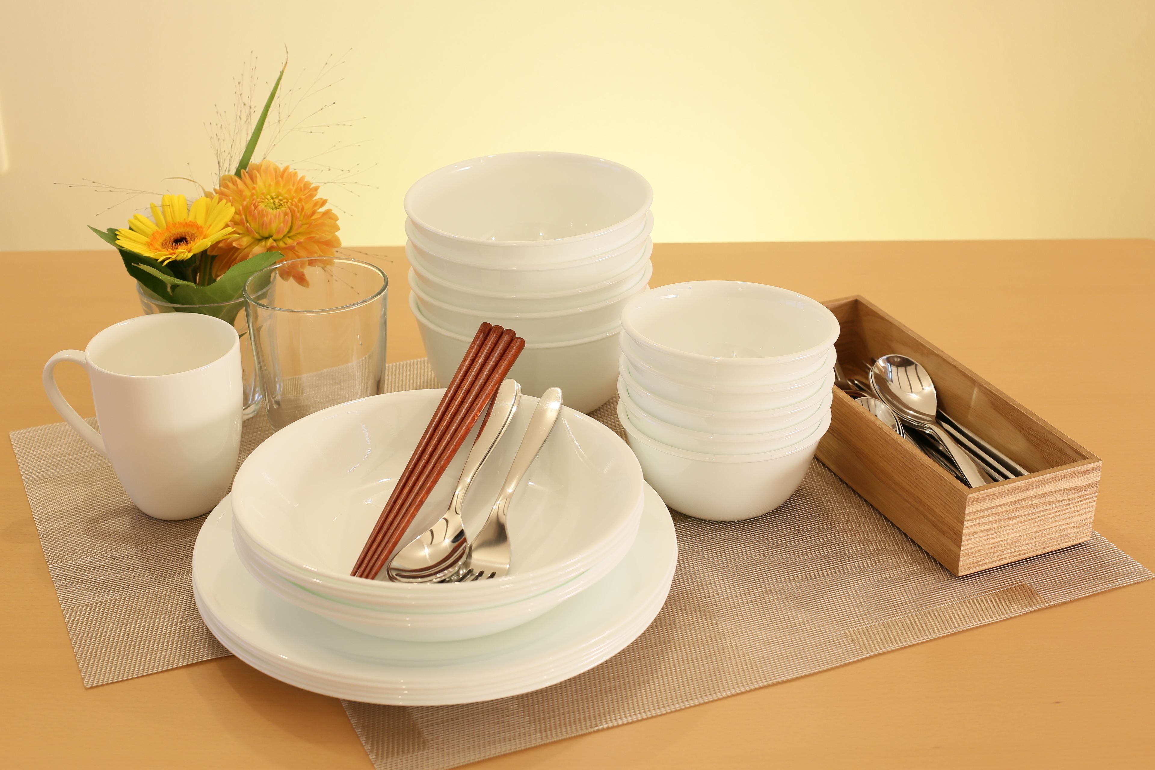 A table set with white plates, bowls, a cup, a glass, chopsticks, and a wooden tray with utensils.