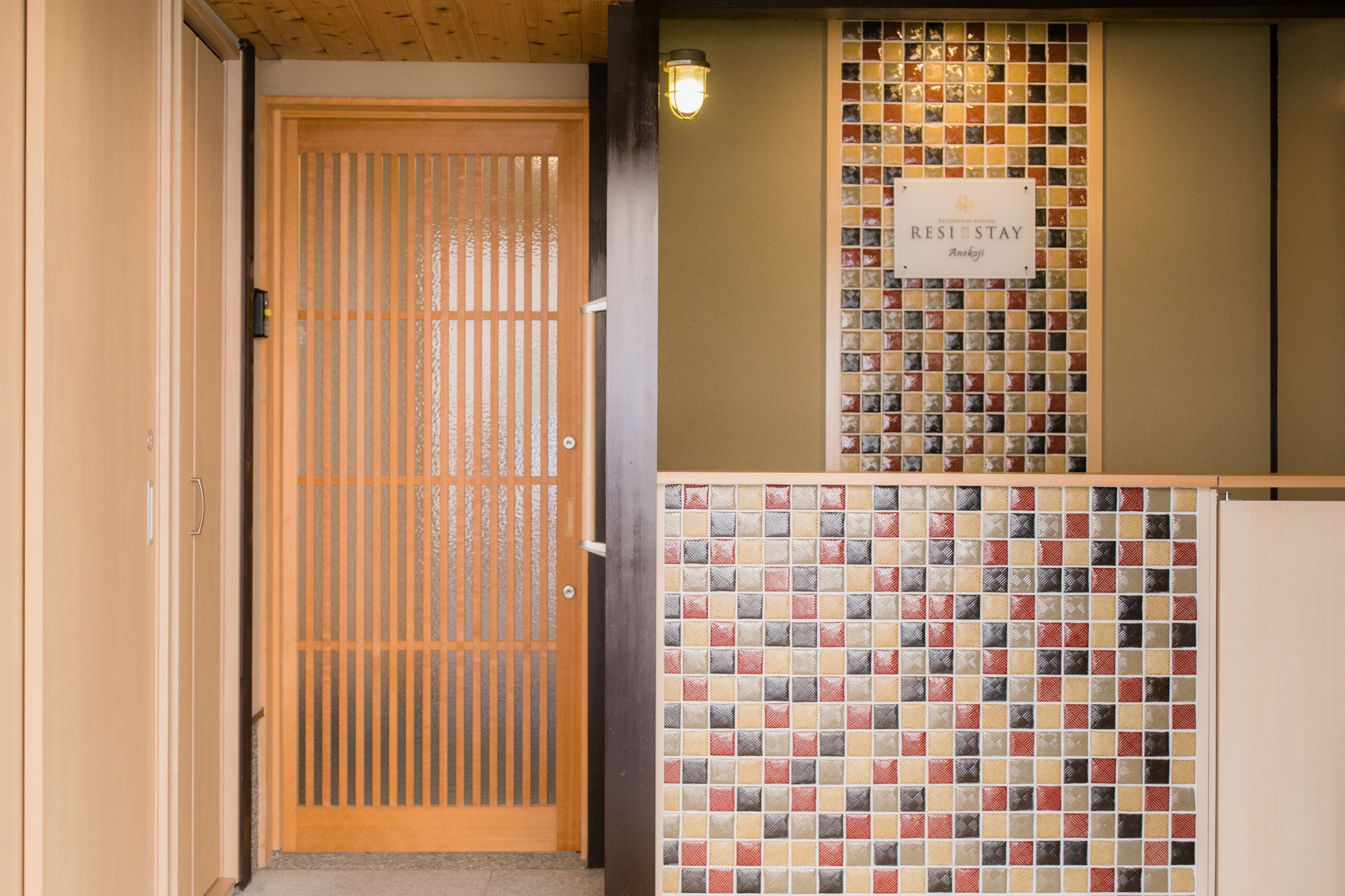 Een hotelentree met een houten schuifdeur, een muur met een mozaïek tegelontwerp, en een bord waarop 