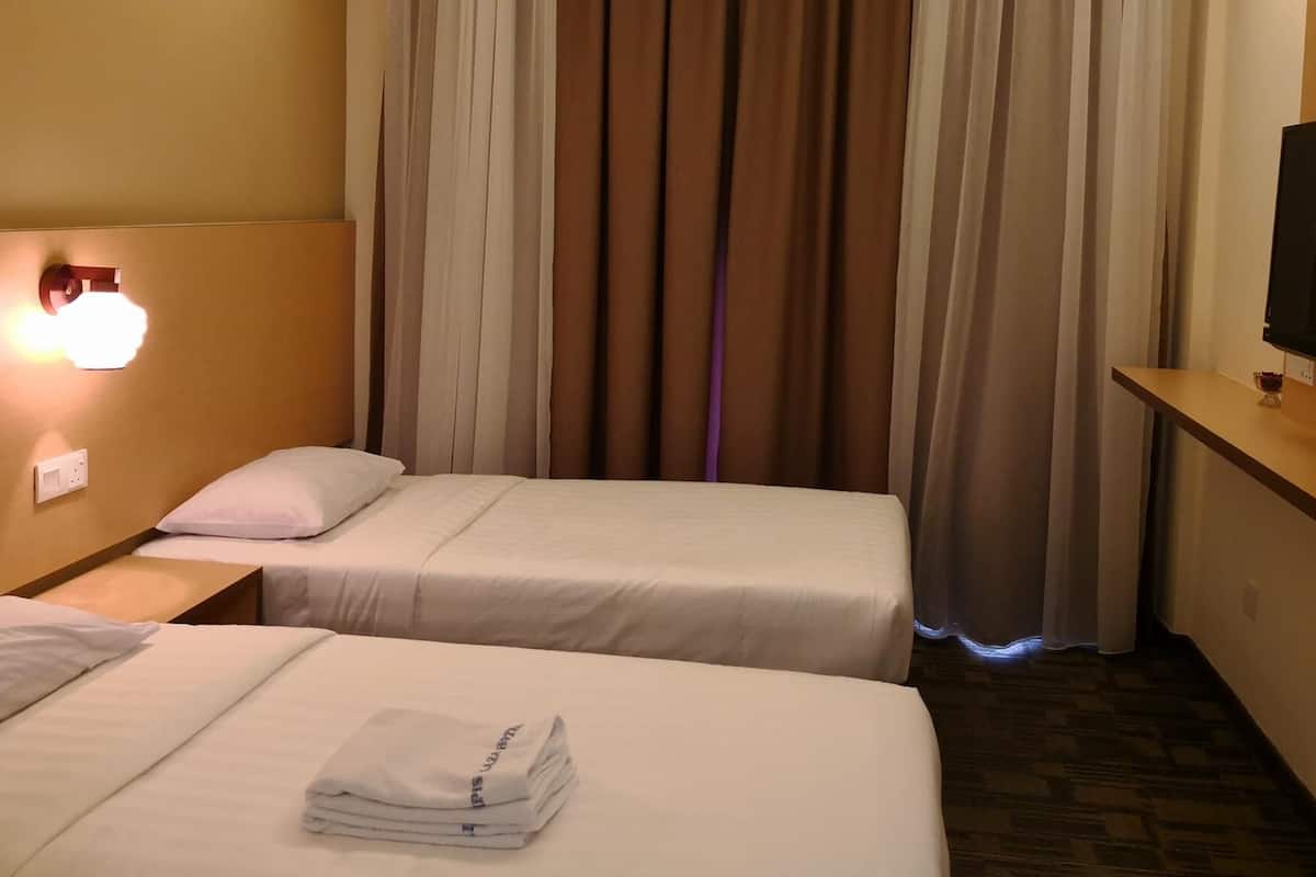 A hotel room with two beds, a TV on a wooden shelf, and a wall-mounted light.