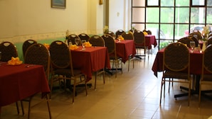 A dining area with multiple tables covered in red tablecloths, arranged in rows with chairs. - Lipis Plaza Hotel (Kuala Lipis)