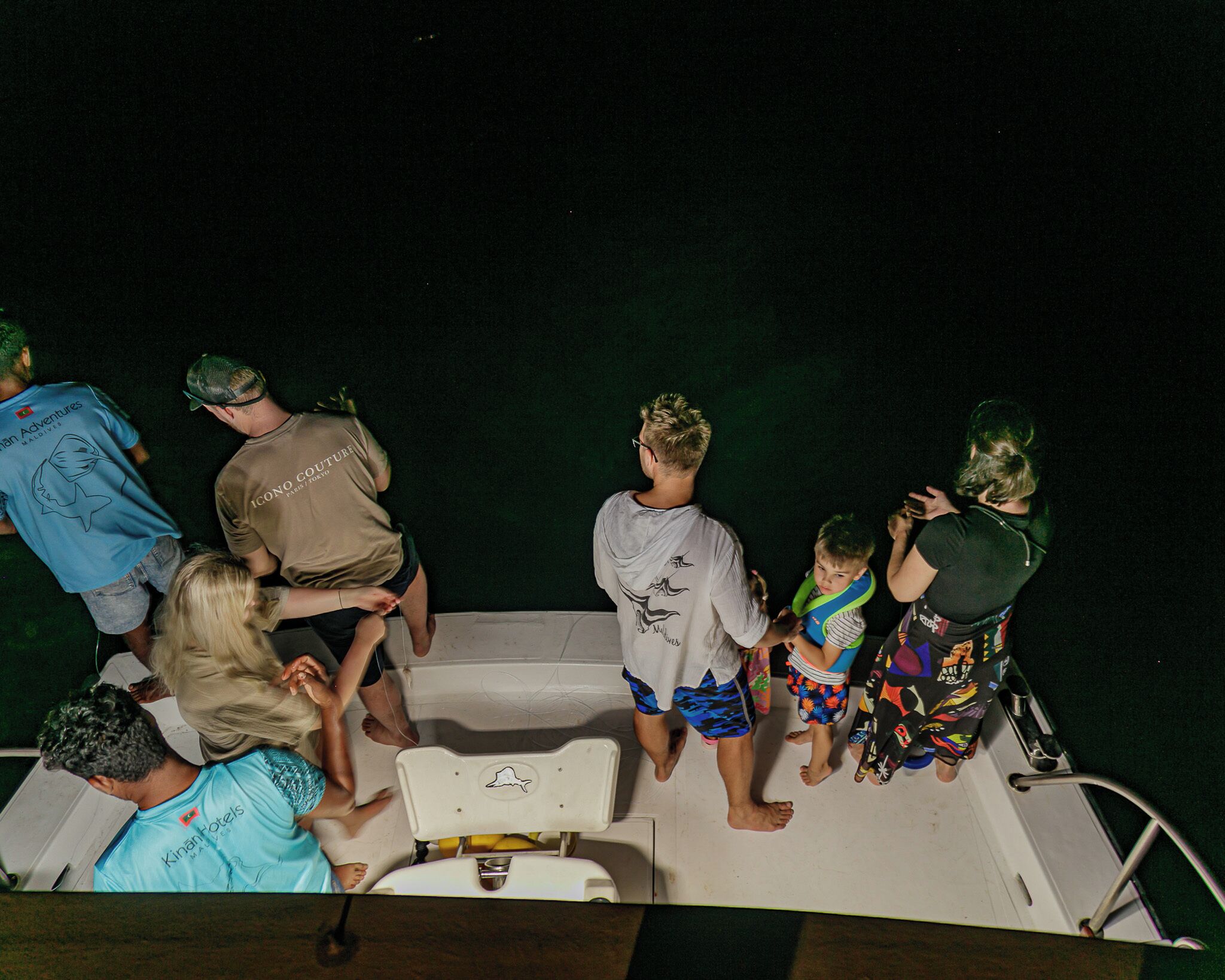A group of people on a boat with a wakeboarder in the center.