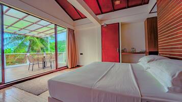 Une chambre moderne avec un grand lit, une porte-fenêtre coulissante donnant sur un espace extérieur aménagé avec des chaises, et une porte rouge.