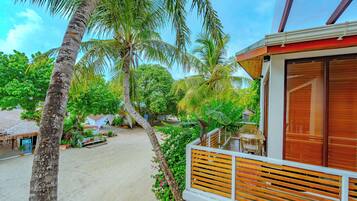 A beachfront property with a wooden deck, palm trees, and a thatched-roof building.