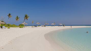 Una playa con aguas turquesas cristalinas, arena blanca y palmeras.