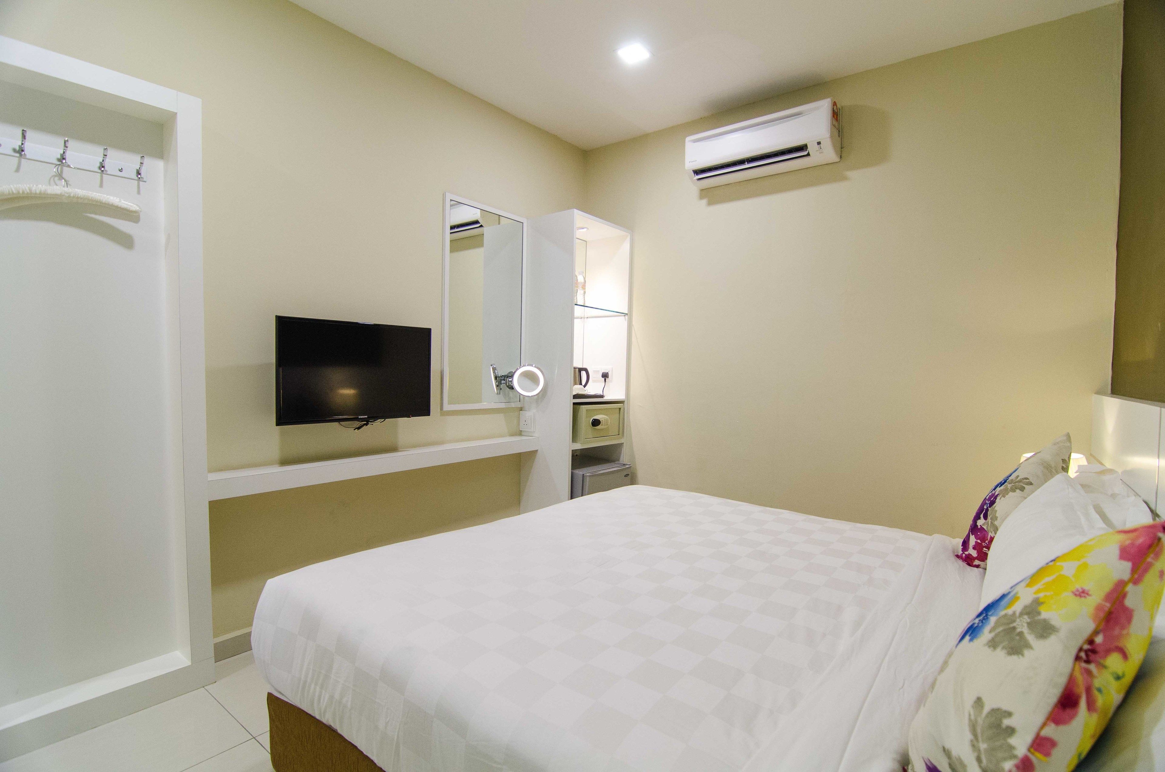 A hotel room with a bed, a television, a mirror, a wardrobe, and an air conditioning unit.