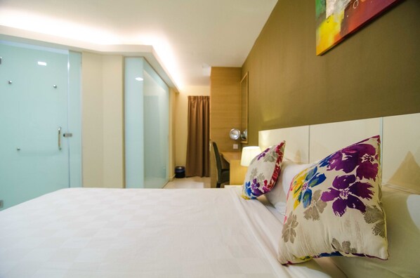 A hotel room with a bed, a desk, a chair, and a door.
