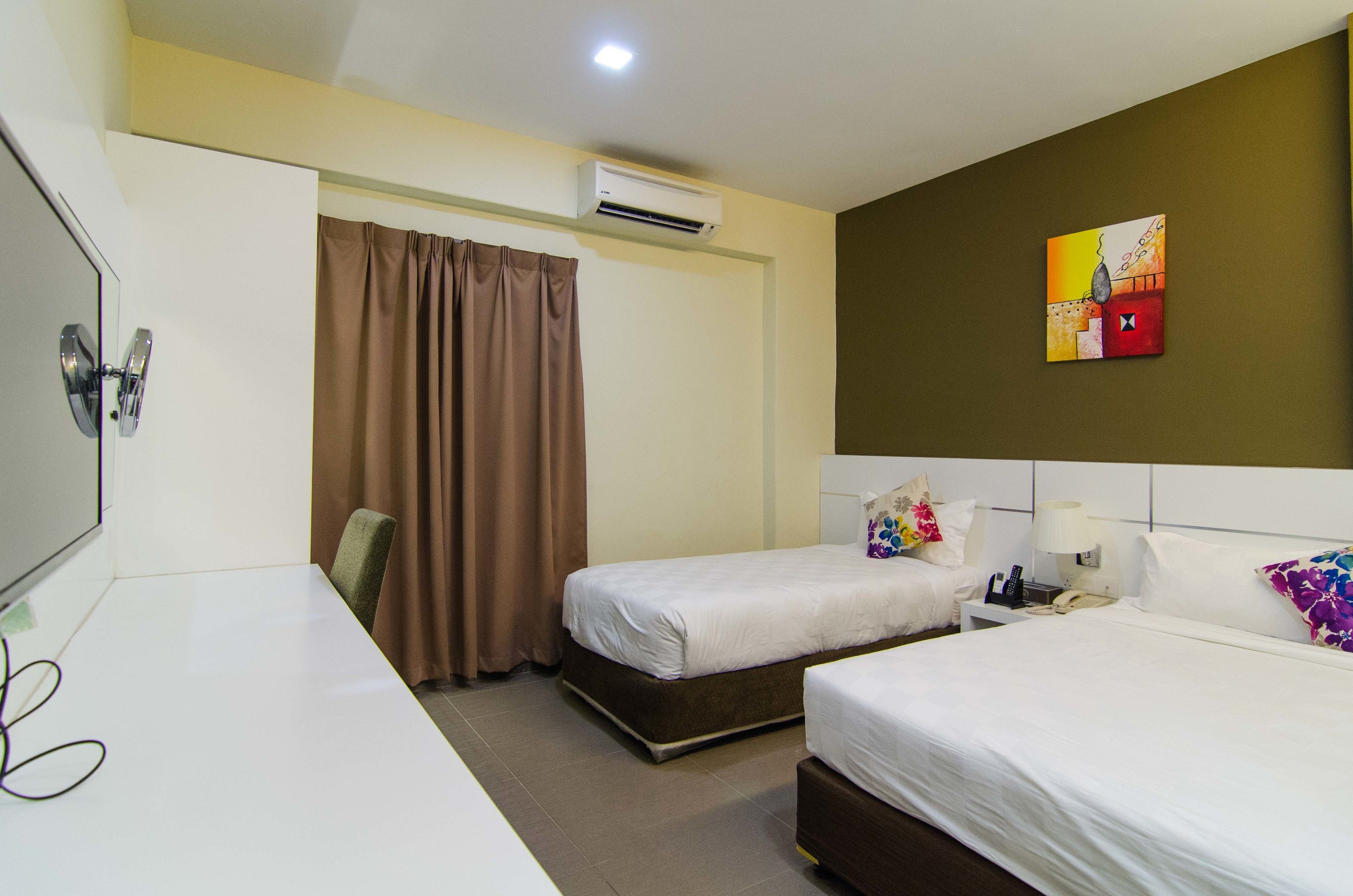 A hotel room with two beds, a desk, a chair, an air conditioning unit, a painting on the wall, and a curtain.