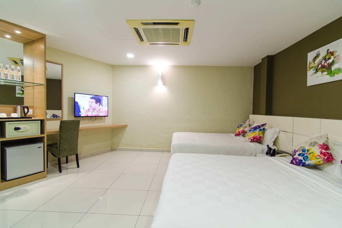 A hotel room with a desk, chair, television, two beds with floral pillows, and a small refrigerator.