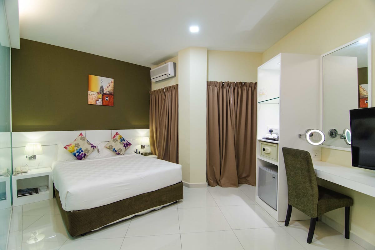 A hotel room with a bed, a desk with a chair, a mirror, and a wall-mounted air conditioner.