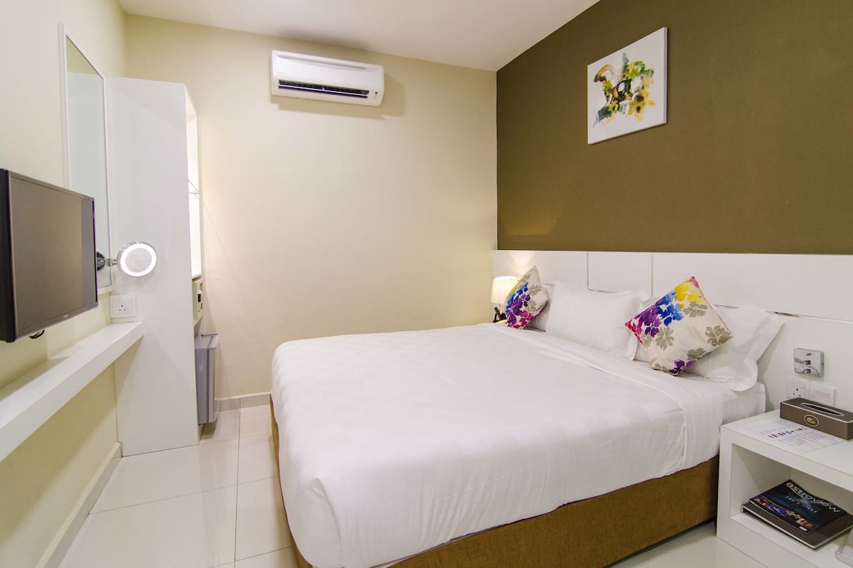 A hotel room with a bed, bedside table, TV, air conditioning unit, and a wall-mounted artwork.