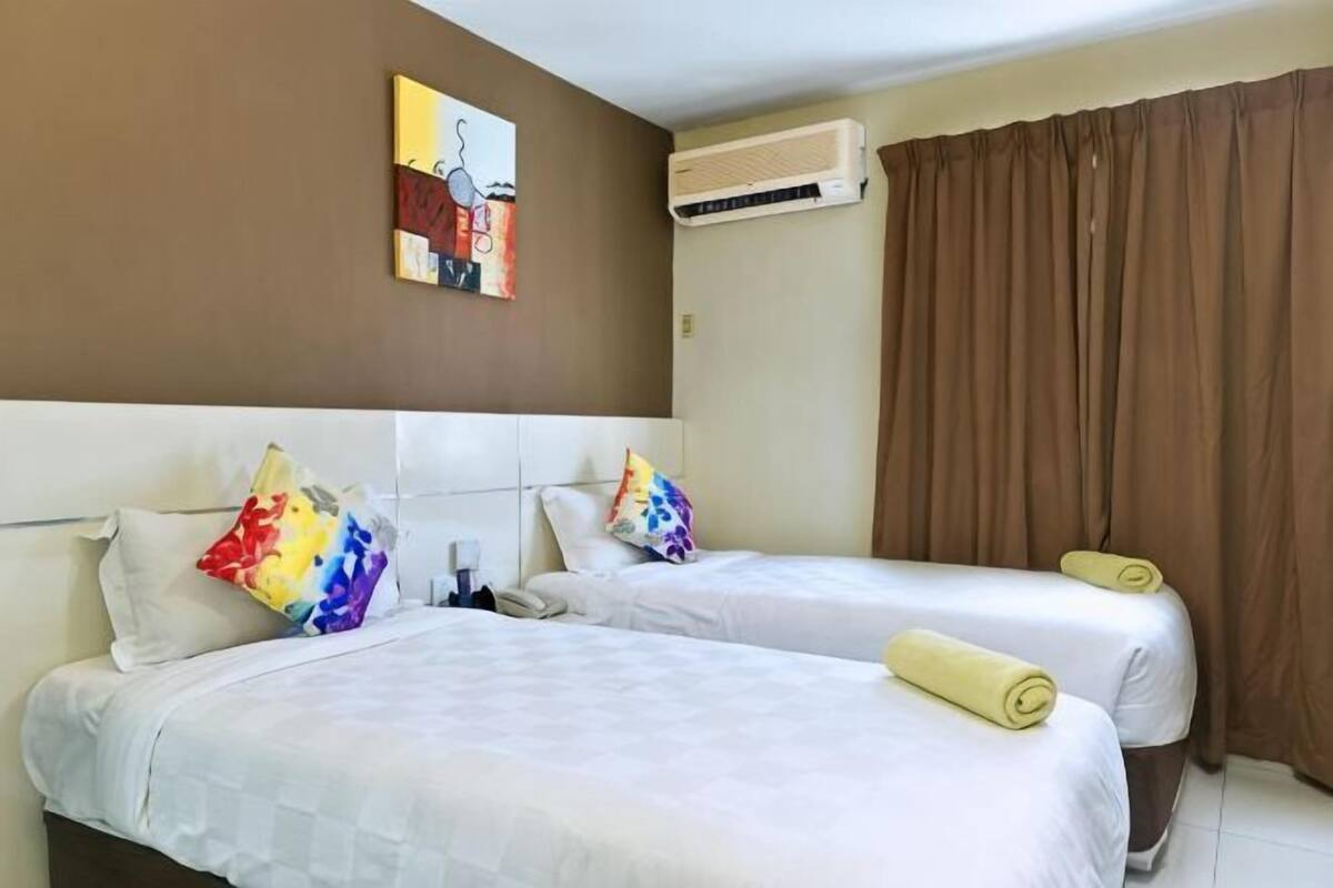 A hotel room with two beds, a painting on the wall, an air conditioning unit, and brown curtains.