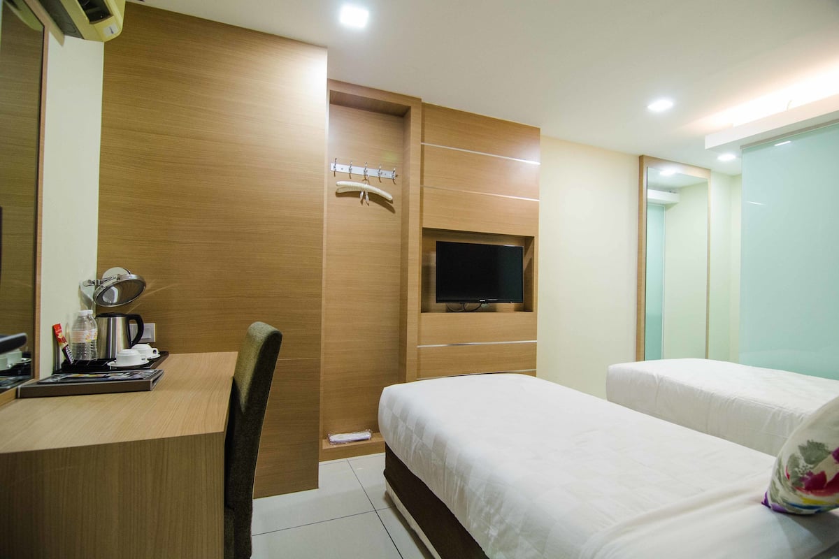 A hotel room with a wooden desk, a television mounted on the wall, two beds, and a mirror.