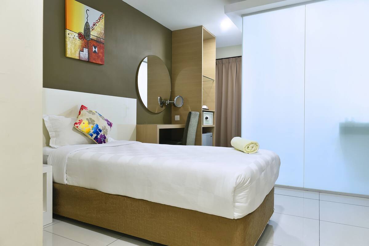 A hotel room with a bed, a desk, a chair, a mirror, and a window with curtains.