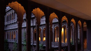 Ein architektonischer Korridor mit aufwendigen Bögen und Säulen, der eine Reihe kleiner, beleuchteter Räume zeigt.