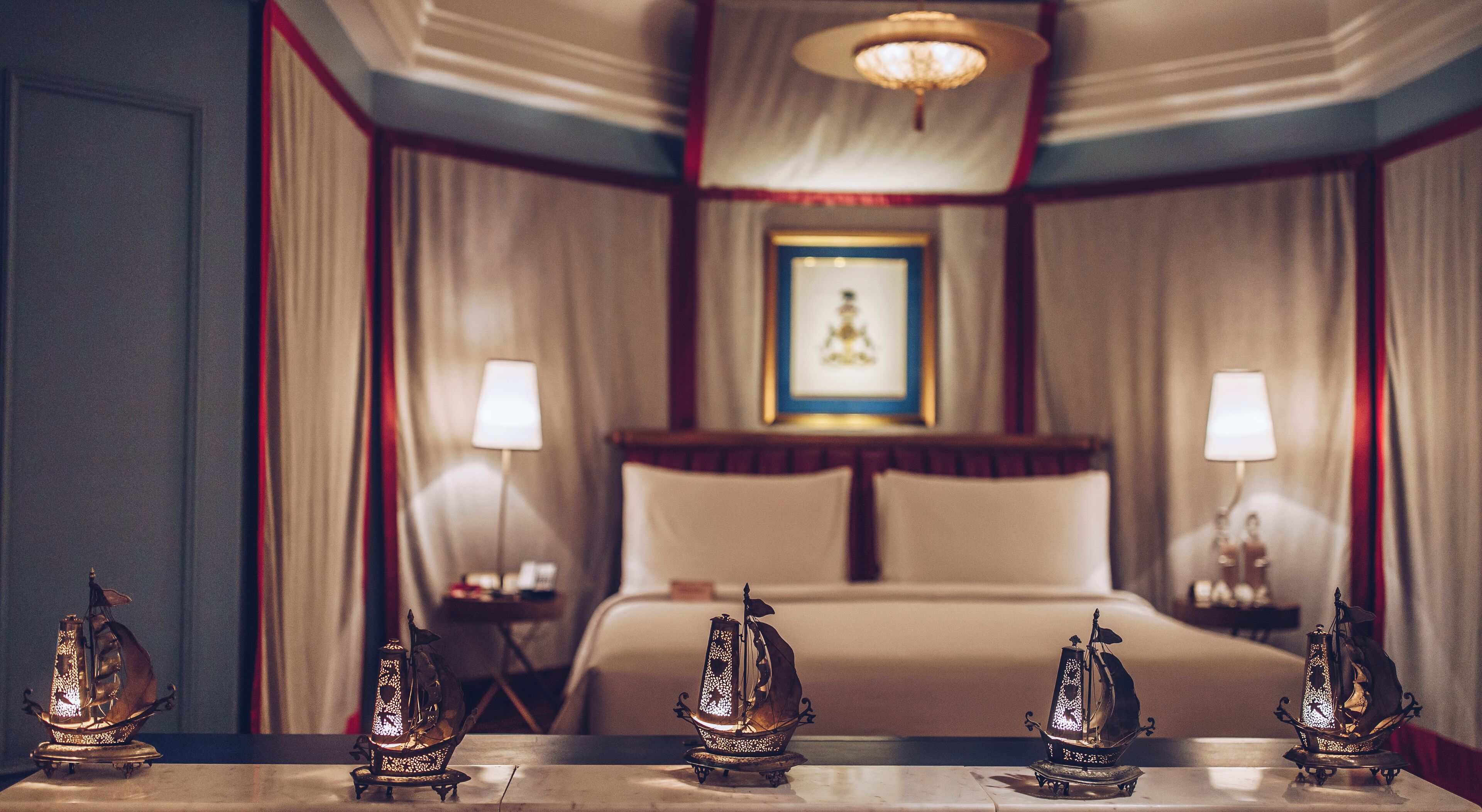 Une chambre d’hôtel avec un lit, deux lampes de chevet et trois modèles de bateaux décoratifs posés sur la table.