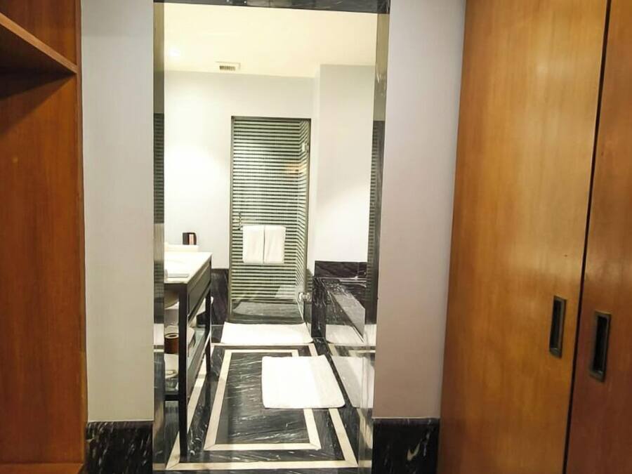 Een gang met een houten garderobe aan de rechterkant, een zwart-wit marmeren vloer, en een badkamer met een gestreept douchegordijn op de achtergrond.