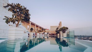 Ein Dachpool im Infinity-Stil mit freiem Blick auf die Stadtlandschaft, umgeben von Liegestühlen und Topfpflanzen.