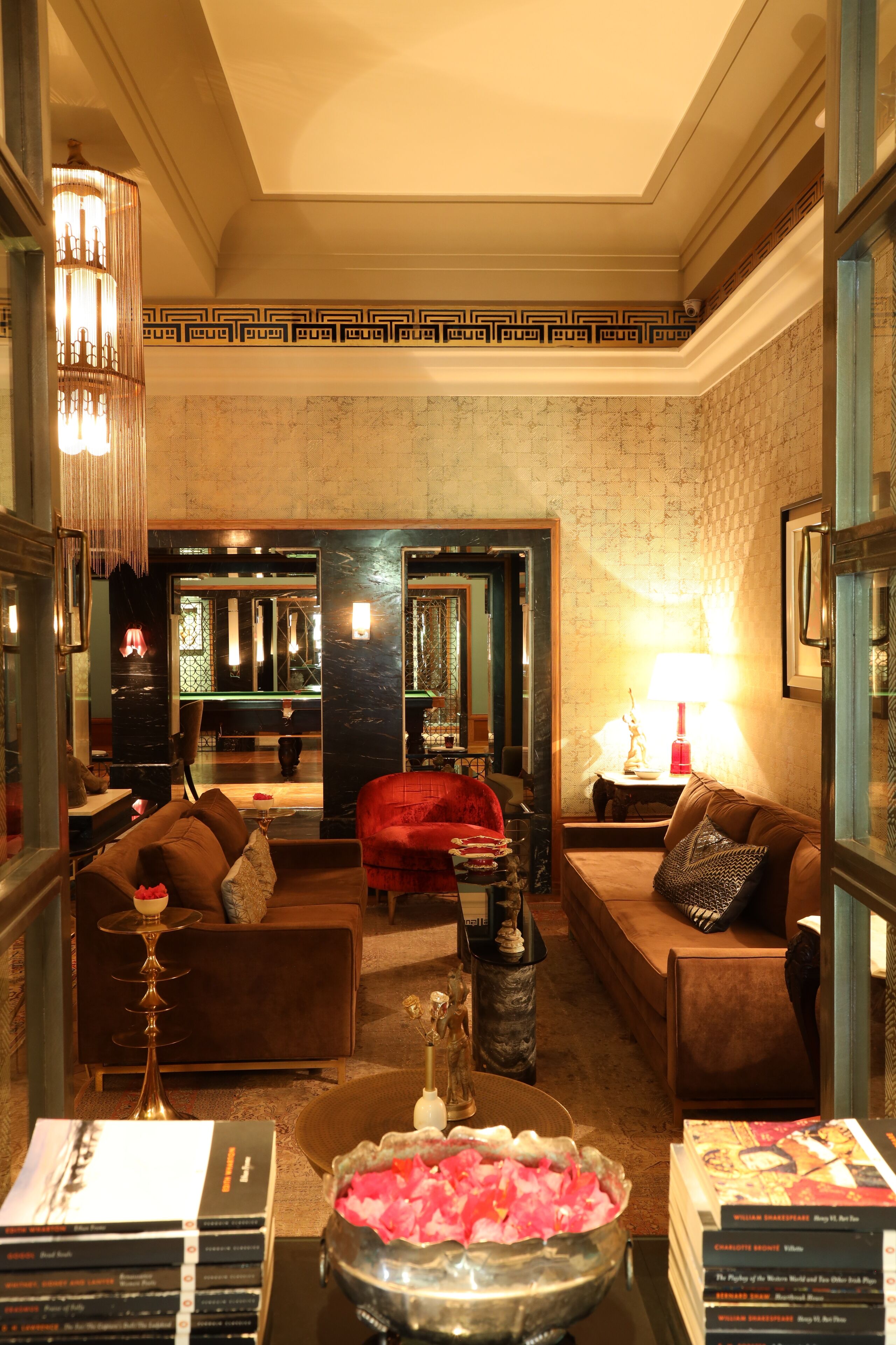 A spacious lobby with a billiards table, leather sofas, a coffee table with decorative items, and a chandelier.