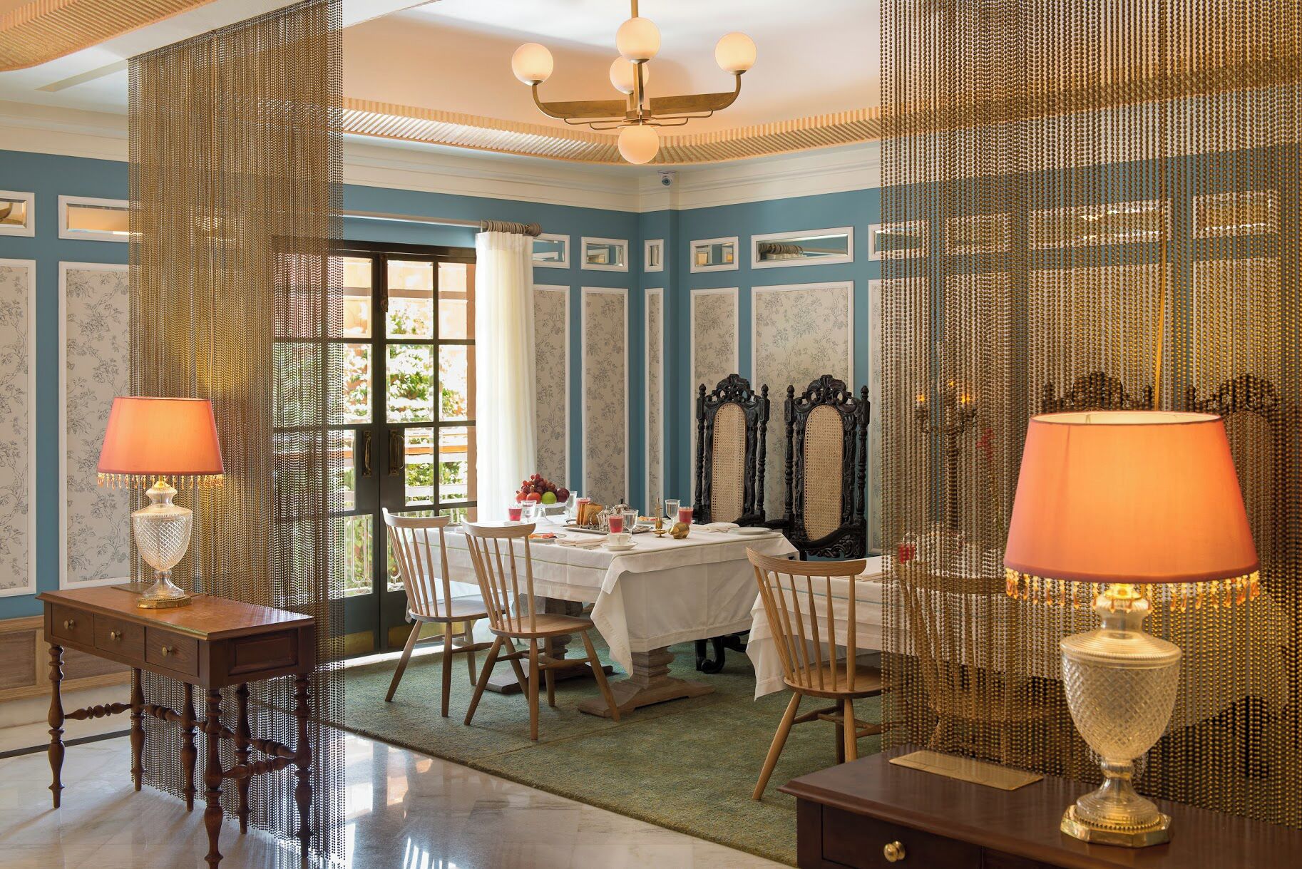 A dining room with a table set for four, surrounded by chairs, a chandelier, and decorative mirrors.