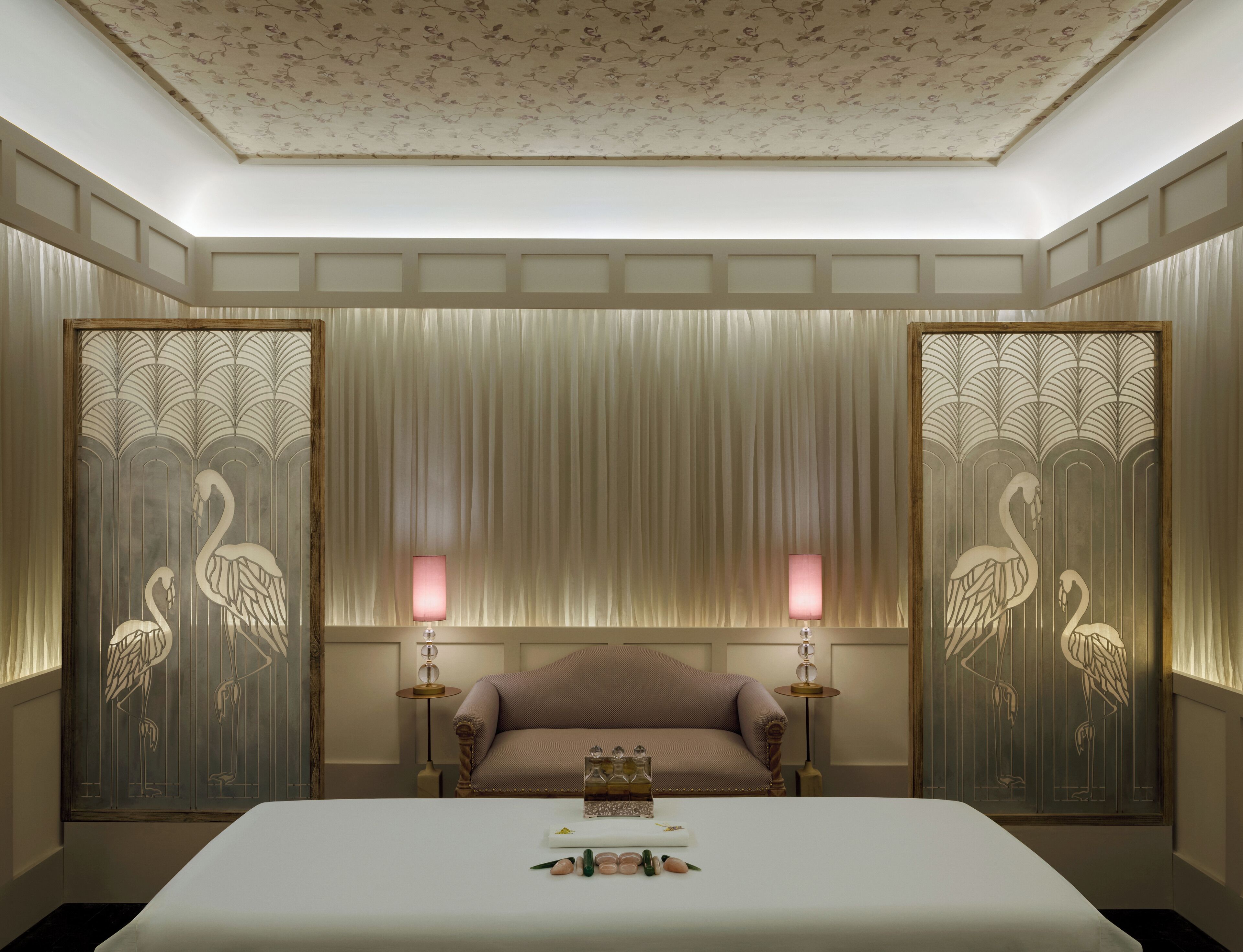 Een hotelkamer met een groot bed, twee lampen, een bank en decoratieve panelen met zwanenmotieven.