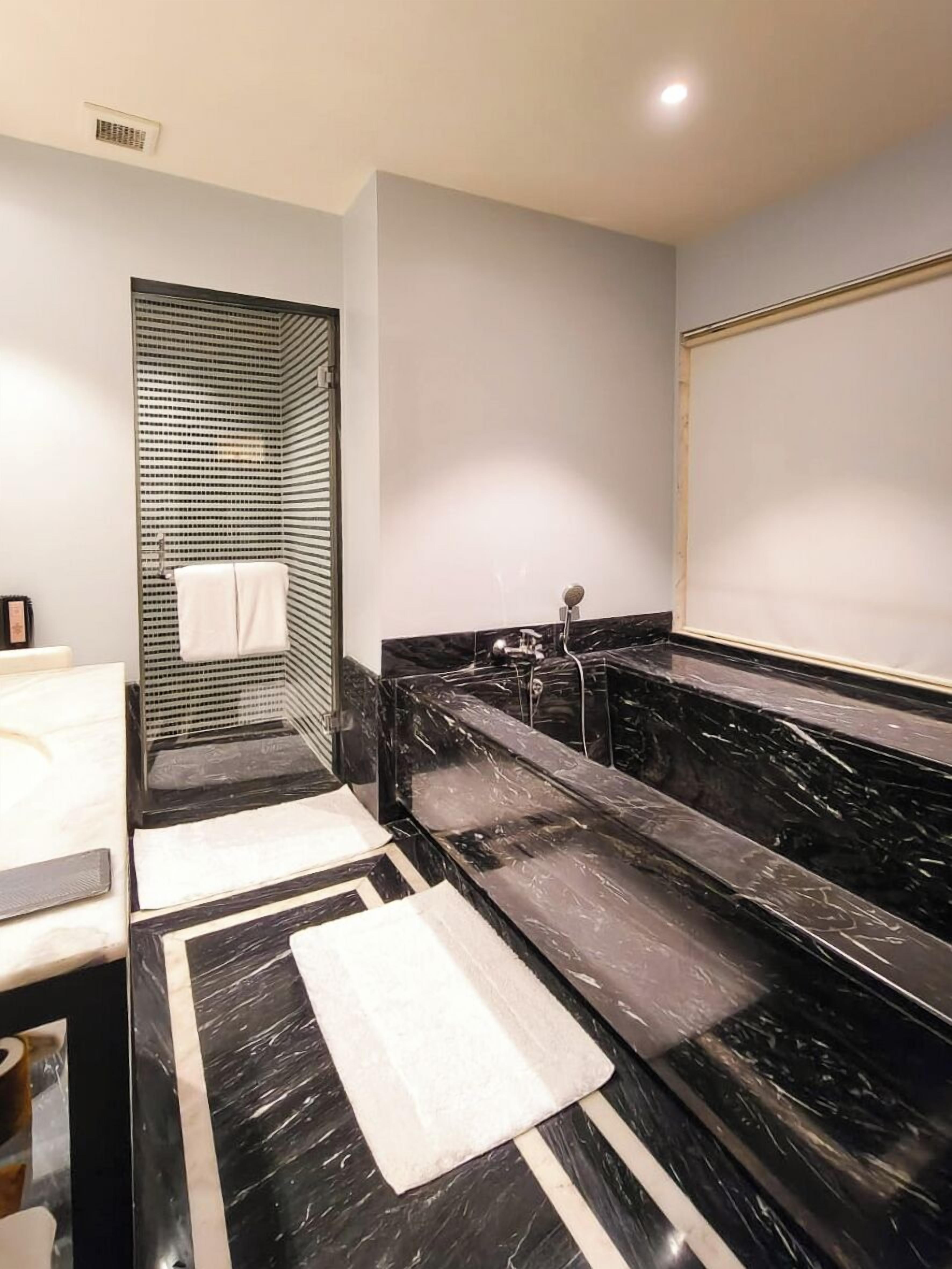 Un baño moderno con tocador de mármol negro, cabina de ducha de cristal y una toalla blanca colgada en la pared.