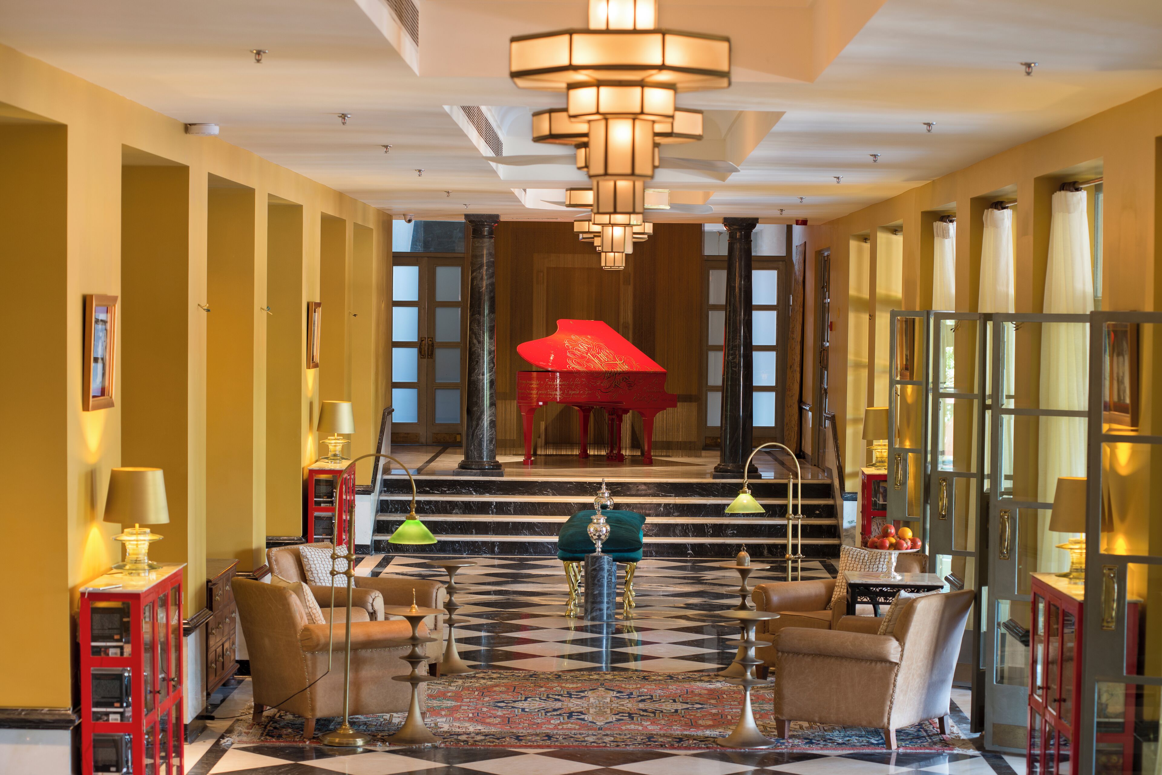 A grand lobby with a checkered floor, a grand piano, and a chandelier.