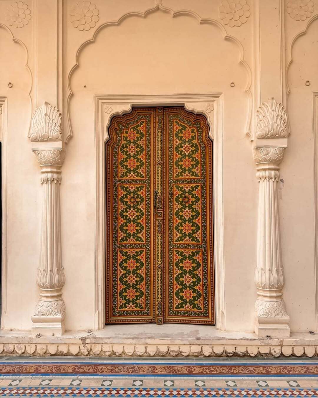 A traditional ornate door with intricate floral patterns, flanked by two white columns with detailed capitals.