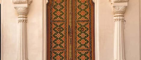 A traditional ornate door with intricate floral patterns, flanked by two white columns with detailed capitals.