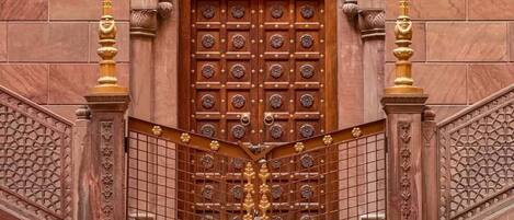 A grand wooden door with intricate carvings, flanked by ornate golden pillars and a decorative metal gate.
