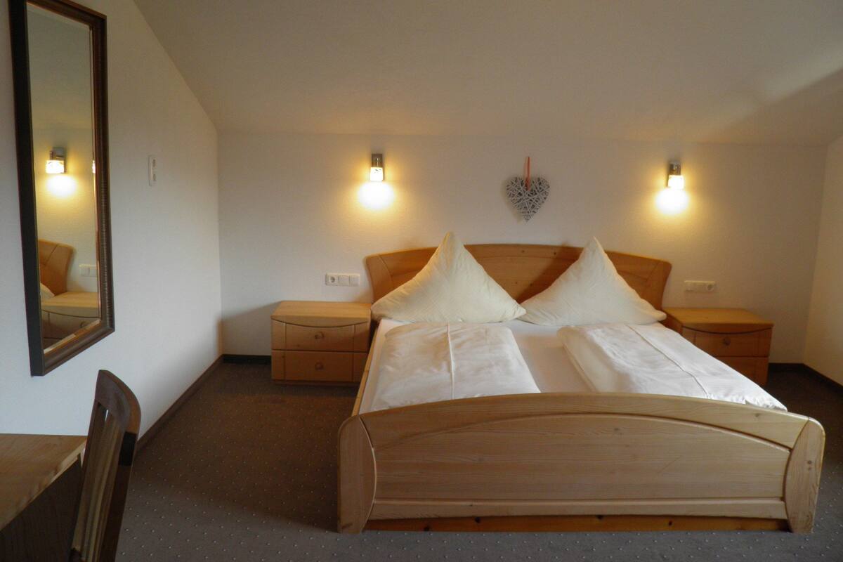 Une chambre à coucher avec un lit en bois, deux tables de chevet, une commode, un miroir et deux lampes fixées au mur.