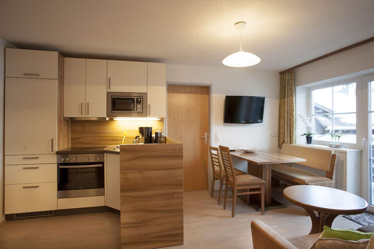 Une cuisine moderne équipée d’un four à micro-ondes, d’un four et d’un îlot central en bois. On y trouve également un coin repas avec une table et des chaises, ainsi qu’un téléviseur fixé au mur.