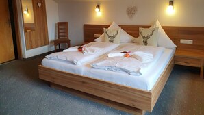 A double bed with white linens, two pillows with deer designs, a wooden nightstand, and a wall-mounted light fixture. - Alpenhof Waengle (Waengle)