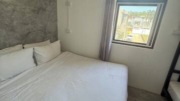 A bedroom with a large bed, a window with a view of buildings, and a grey textured wall.