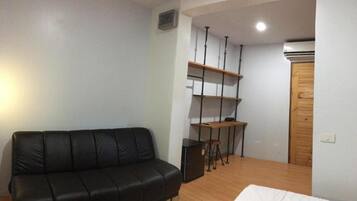 A small, modern room with a black leather sofa, a wooden desk with shelves, and a wooden wardrobe.