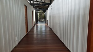 A long, narrow corridor with white walls and a wooden floor, leading to an open area with natural light. - Us Hostel Samui (Koh Samui)