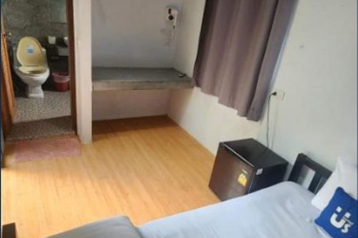 Habitación de hotel con cama, mesita de noche, lámpara colgante, zona de ducha y un inodoro visible a través de una puerta abierta.
