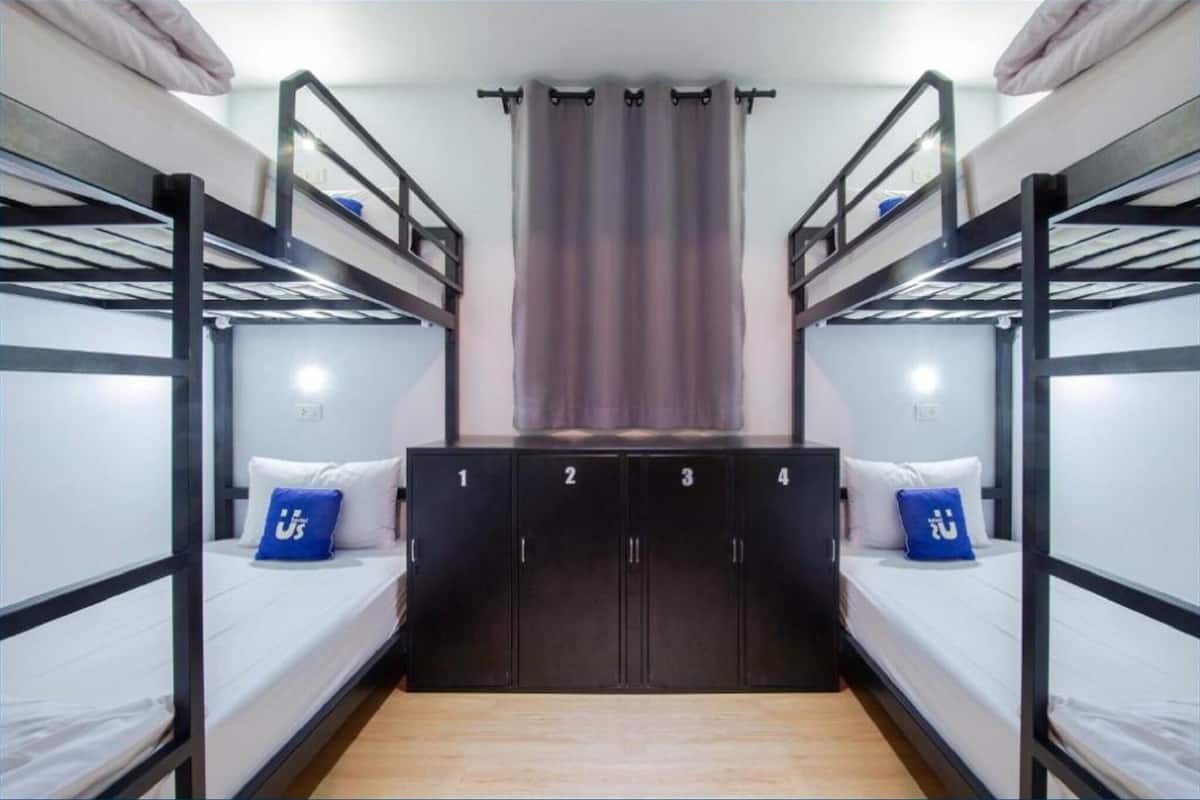 Une chambre avec un lit superposé, un grand placard au centre, un rideau et un lit avec un oreiller.