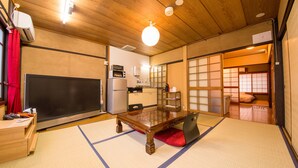 A traditional Japanese room with tatami flooring, a wooden table, a television, and a kitchen area. - Rin Kyoto (Kyoto)