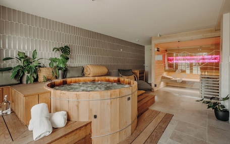 A modern spa area with a wooden hot tub, wooden flooring, and a seating area with cushions.