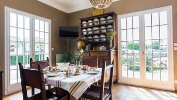 A dining area with a table set for a meal, surrounded by chairs, a television mounted on the wall, and a large window with a view of the outdoors.