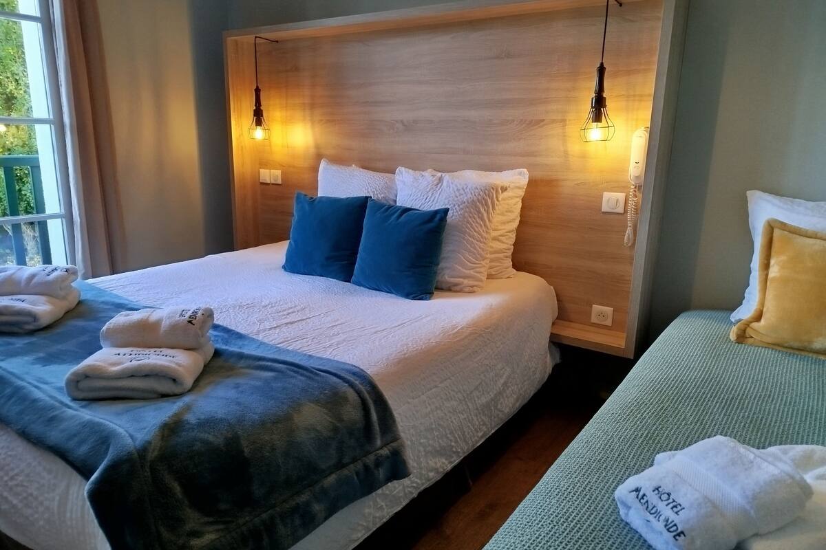 Ein Hotelzimmer mit einem Holzkopfteil, zwei Nachttischlampen, einem Bett mit weißblauer Bettwäsche und einem Nachttisch mit Telefon.