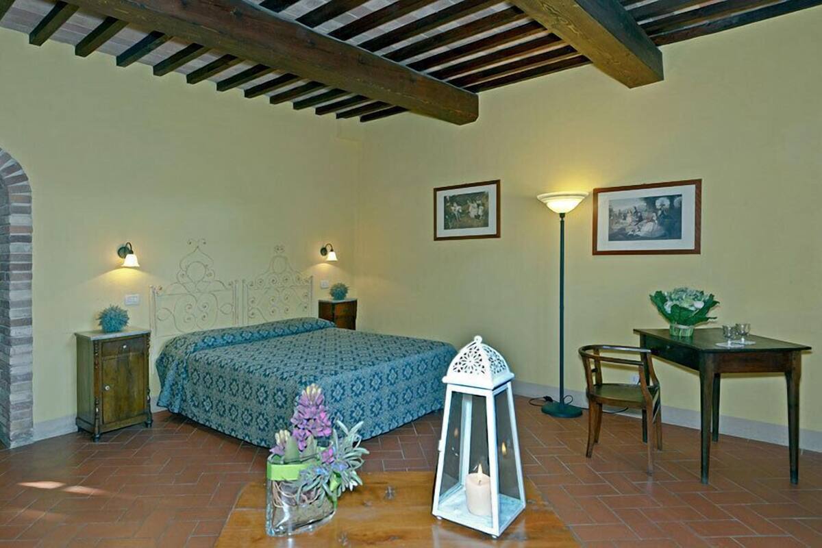 Une chambre à coucher comprenant un lit, deux tables de chevet, un bureau, une chaise, une lampe sur pied et un luminaire fixé au mur.