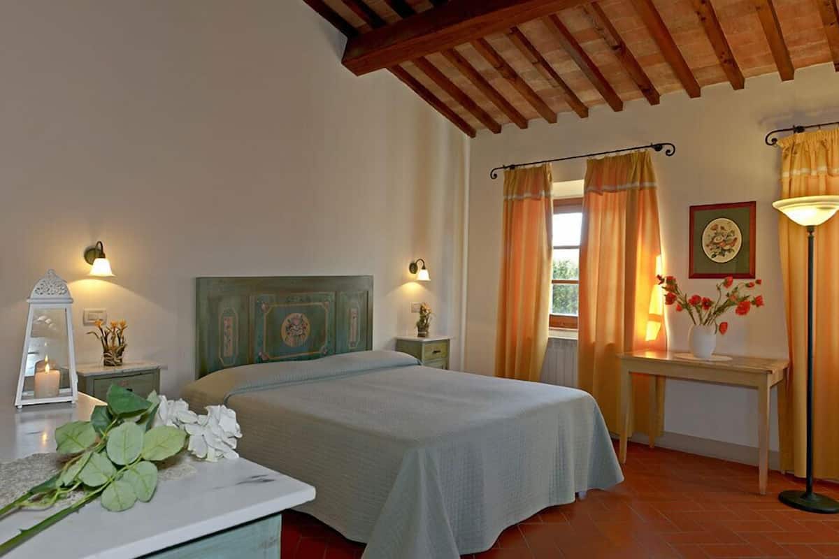 Une chambre à coucher avec un lit, des tables de chevet, une commode, une lampe et des rideaux.